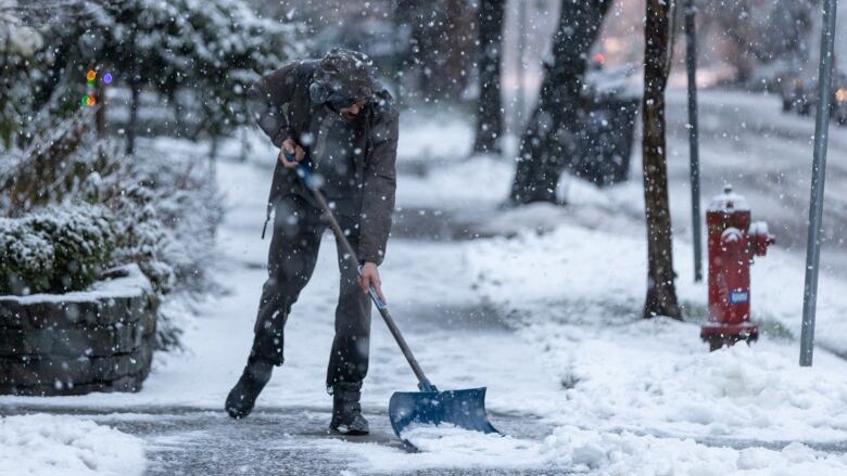 A person shovels snow from a sidewalk in West End, Vancouver as heavy snowfall at dusk turned roads slippery on Jan. 4, 2020. 