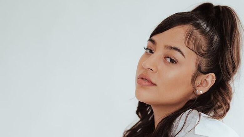 A Black woman is wearing a white shirt standing in front of a white wall