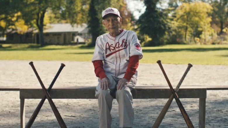 A man sits on a bench wearing a baseball uniform