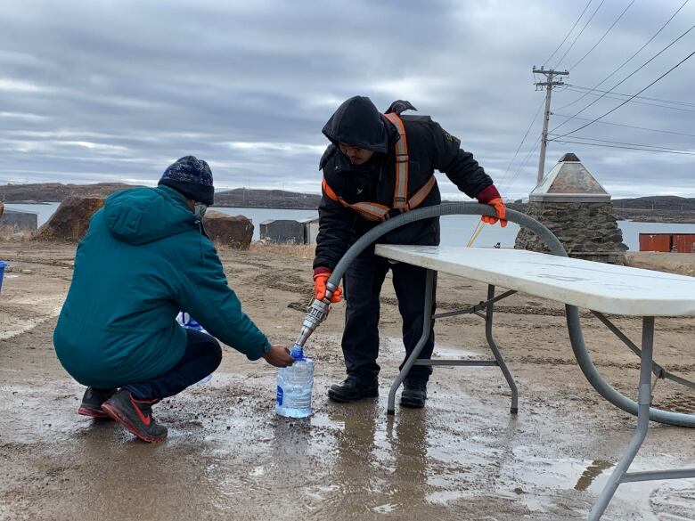 A man fills up another man's water container with treated water from a truck during Iqaluit's water crisis in October 2021. 