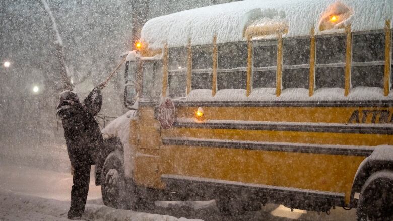 A school bus driver tries to clear snow as a winter storm. 