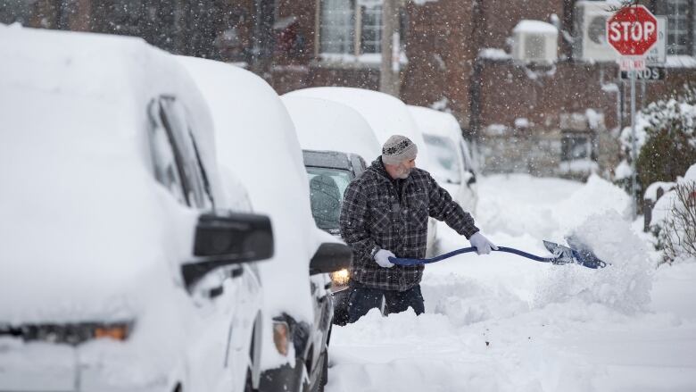 A man digs out a car in Toronto's Beaches neighbourhood after a significant dump of snow on Jan. 17, 2022.