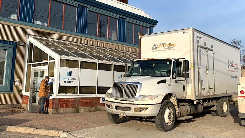 A shredding truck is parked in front of the former Island Employment office as someone scrapes signs off the windows of the building.