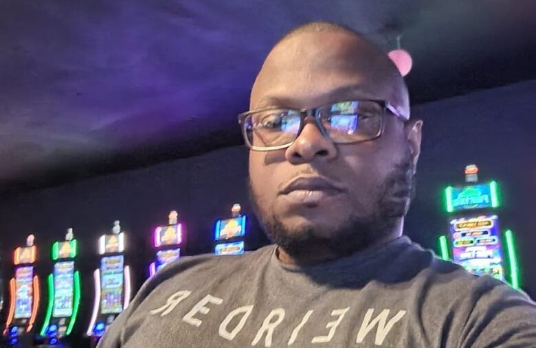 A man with a beard and glasses looks at the camera with what appears to be VLT machines in the background.