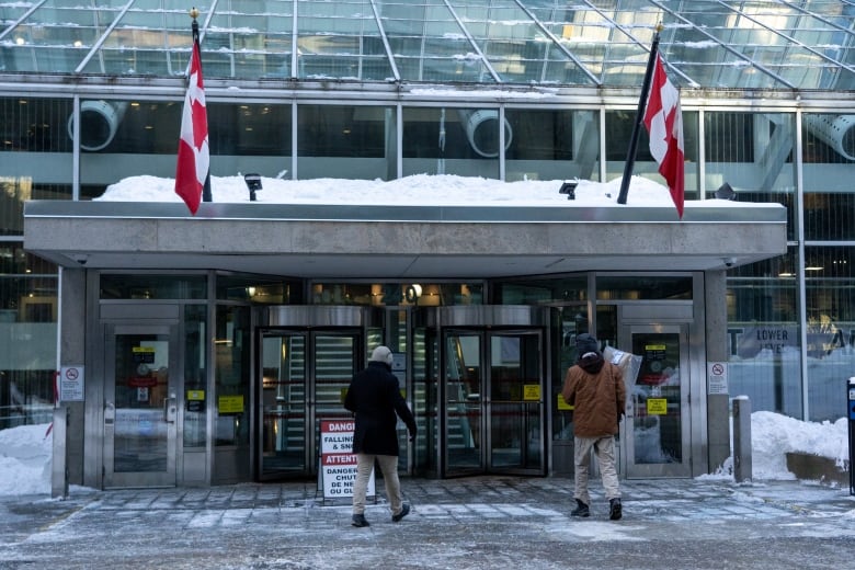 A building with two Canadian flags, and people walking in.