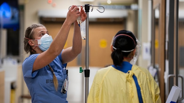 A nurse readies a bag on a hospital stand for a patient.