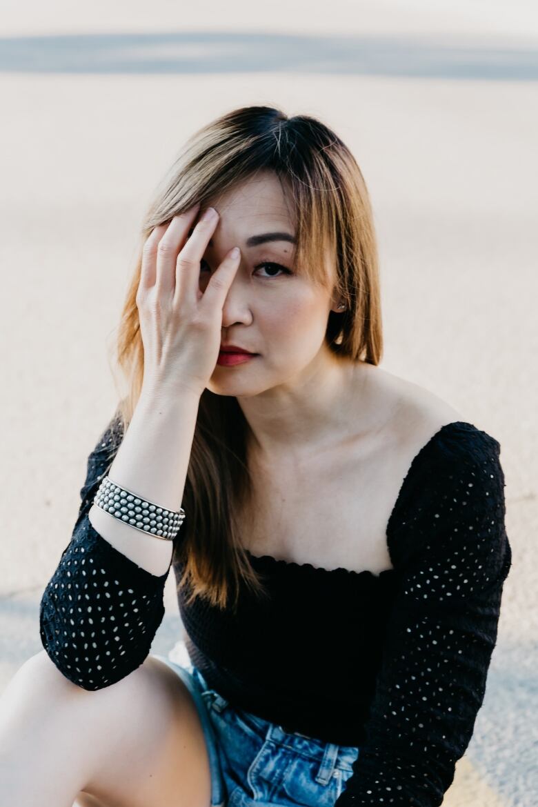 An Asian woman sits in front of the camera, with one hand over her face