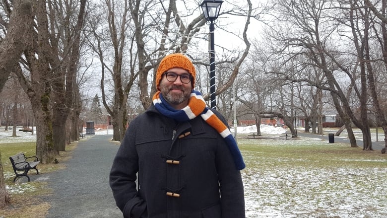 A person wearing a hat and scarf stands on a path in a park. There's some snow on the ground.