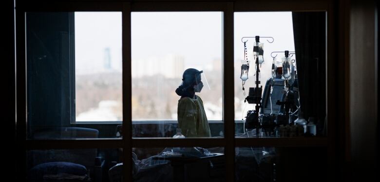 A nurse looks at IV bags and monitors while attending to a patient in the ICU. There is a large window in the background.