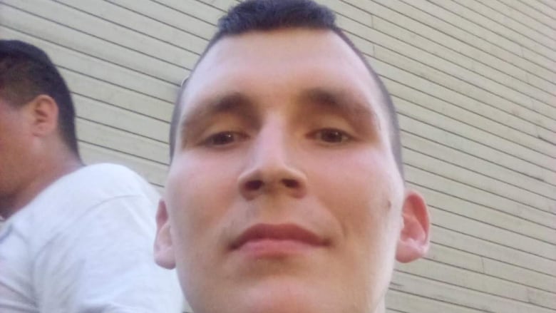 A low-angle selfie of a young man with dark hair cropped close on the sides and slightly longer on top.