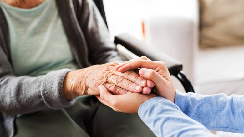 Person holding the hand of an elderly person in a wheelchair.