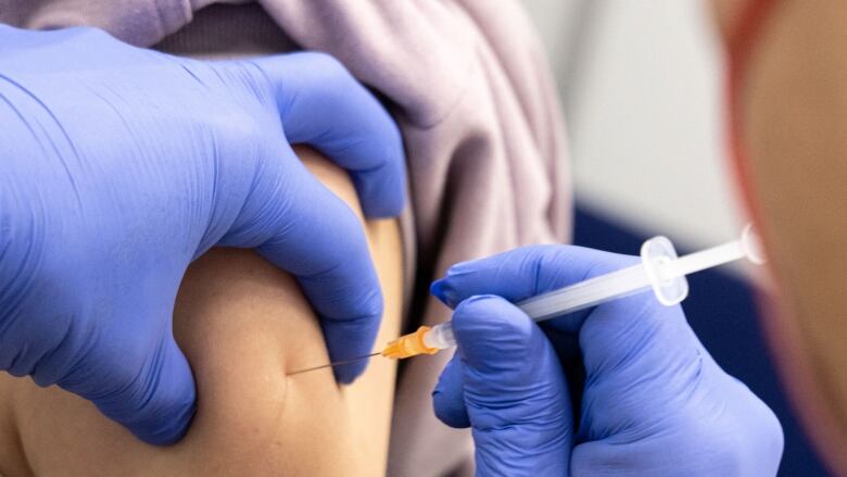 A needle is being pushed into a person's upper arm at a clinic.