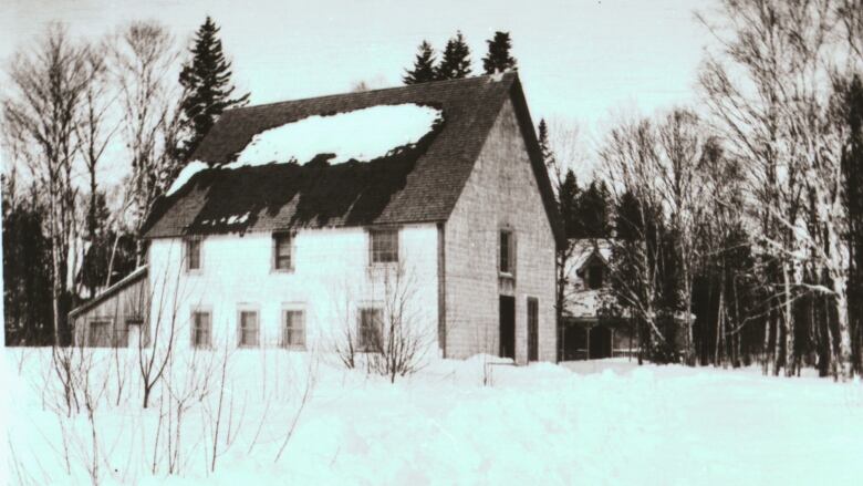 Old black and white photo of a two-story, white-sided building surrounded by snow. 