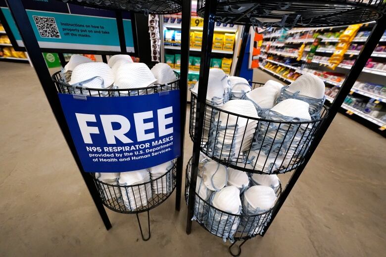 A basket of dozens of free respirator masks. A sign reads 'FREE N95 Respirator Masks, provided by the U.S. Department of Health and Human Services'.