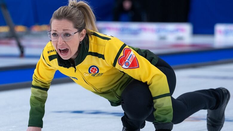 A woman slides on the ice in curling gear. 