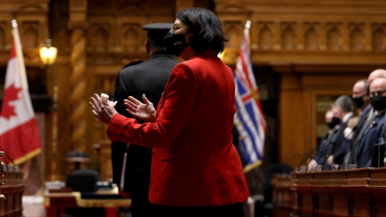 A woman wearing red and a black face mask appears to be speaking to a group