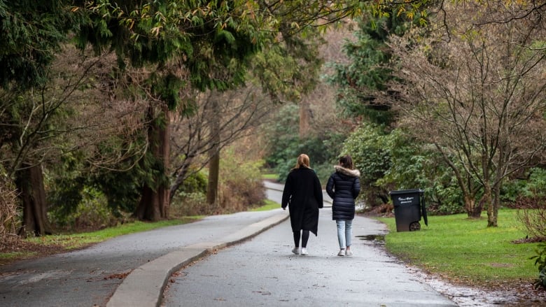 Two people, back to camera, walk down a paved trail in a forested park.