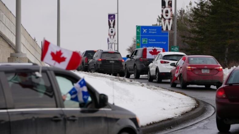 A row of vehicles with Canada flags goes up a curved ramp.