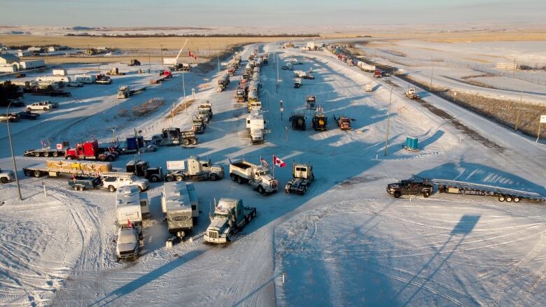 A look from above at tractor-trailers and other large vehicles parked on a snowy prairie highway.