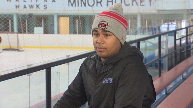 A Black teen in a hockey rink wearing a grey touque and a black jacket