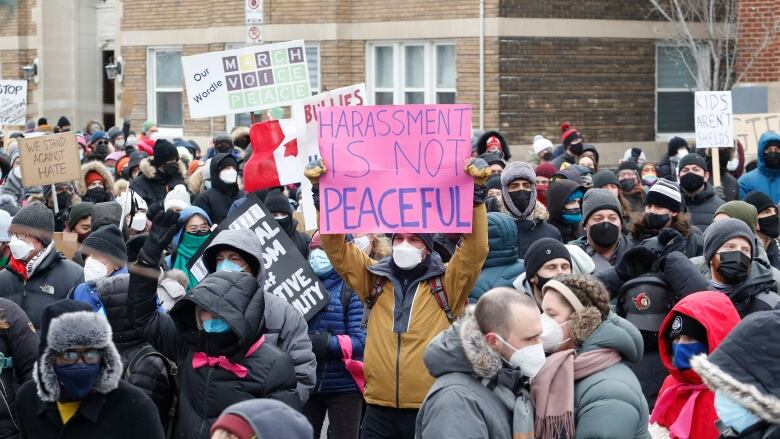 A crowd of people outside in winter coats, some holding signs.