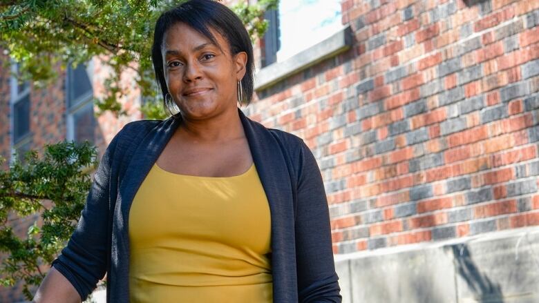 A Black woman with dark hair wearing a yellow tank top under a dark blue cardigan