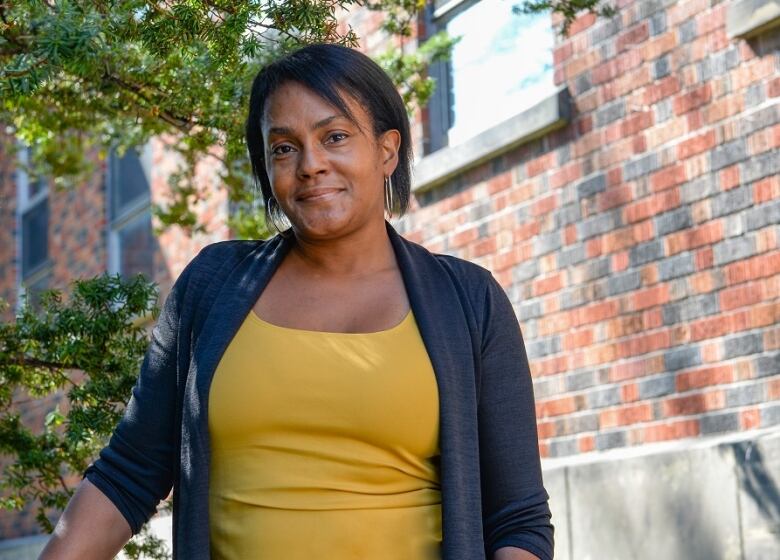 A Black woman with dark hair wearing a yellow tank top under a dark blue cardigan