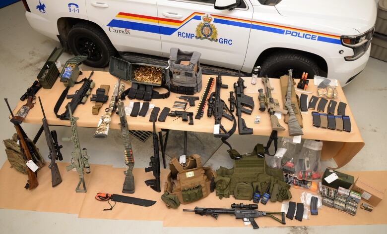 Firearms and ammunition are laid out on a large wooden table.