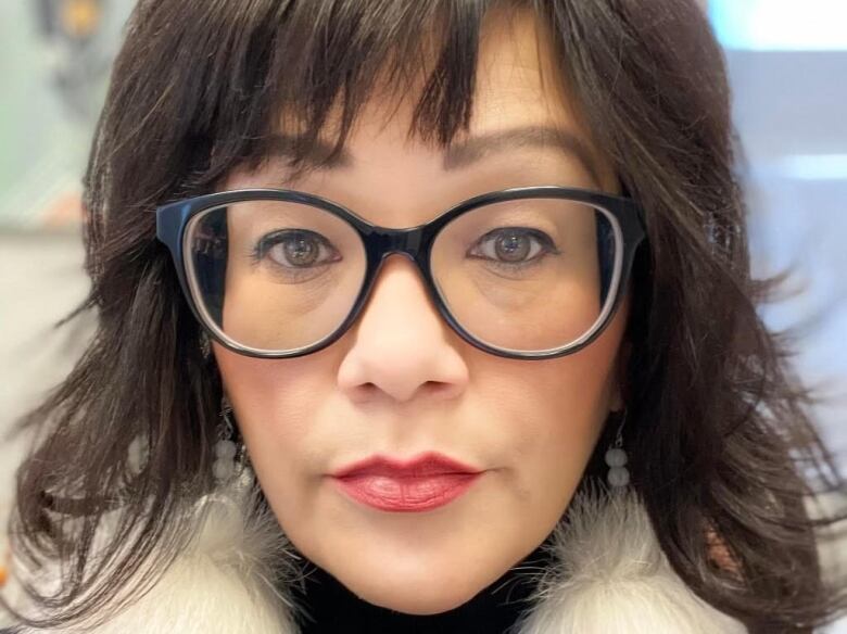 Tight shot of a woman's face staring into the camera, with long dark hair and wearing dark-rimmed glasses.