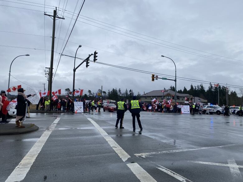 Protesters carrying Canadian flags gather at an intersection.