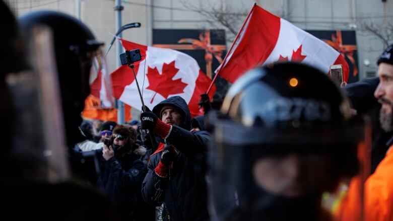 A Freedom Convoy protester uses a camera on a selfie stick as police enforce an injunction against protesters, some who have been camped in their trucks near Parliament Hill for weeks, on Feb. 19, 2022.