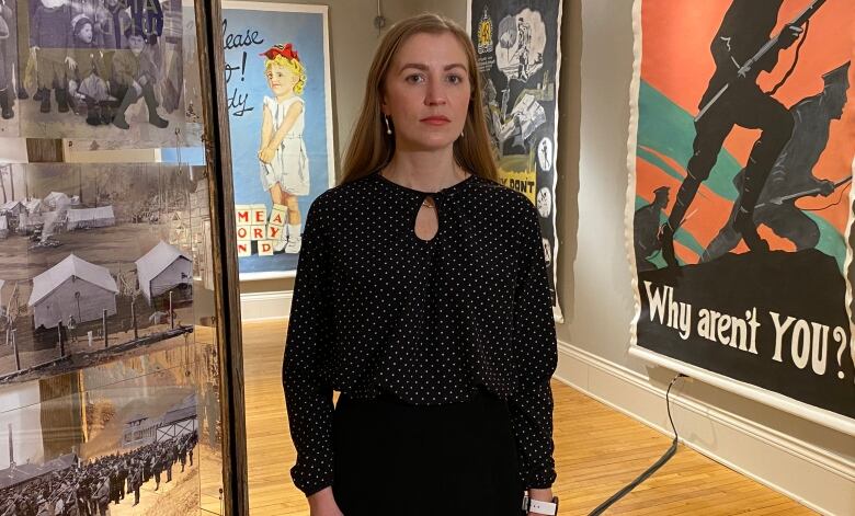 A woman stands in a gallery with posters hanging in the background.