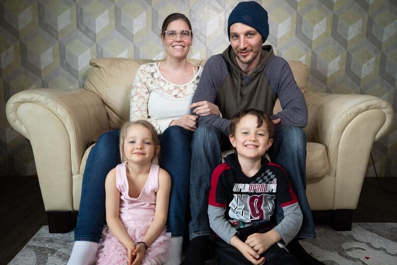 A woman and man sit with their two children on a couch.