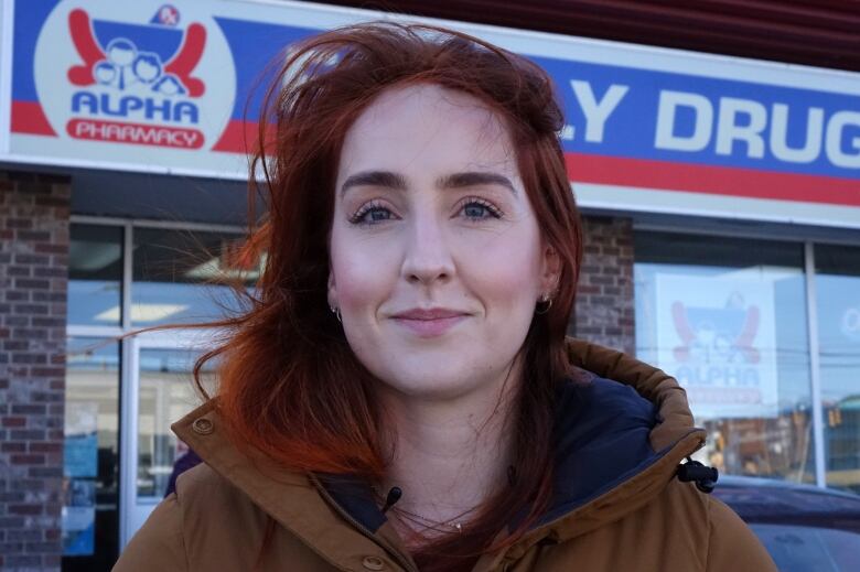 A woman with red hair standing in front of a pharmacy. 