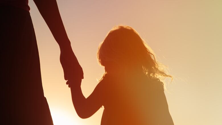 A silhouette of a young child holding their parent's hand.