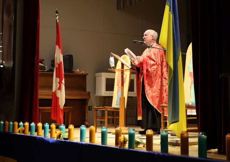 A priest in colourful robes stands at a lectern and leads prayer service inside a Ukrainian Catholic church.