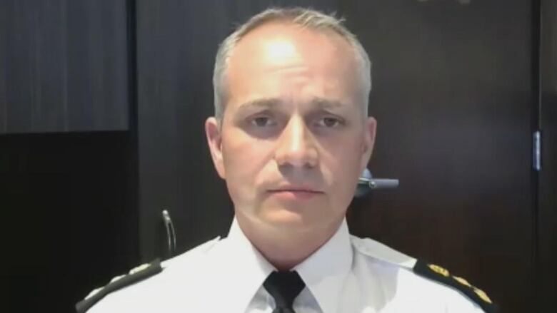 A man with grey hair in a police uniform looks at the camera.