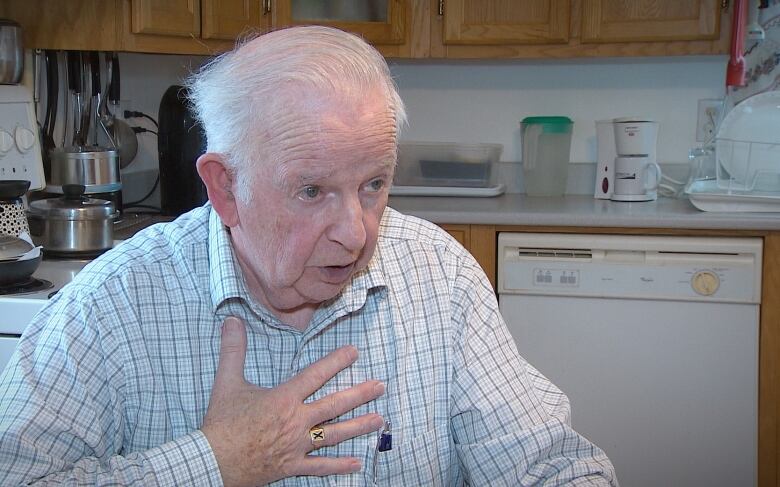 A man with white hair gestures as he talks in his kitchen.