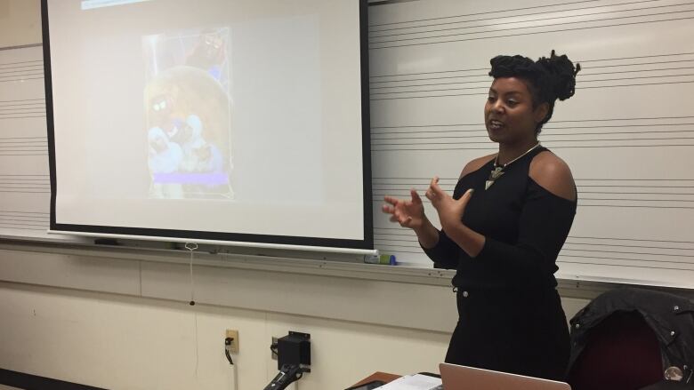 A Black woman standing at the front of a classroom in front of a projector screen