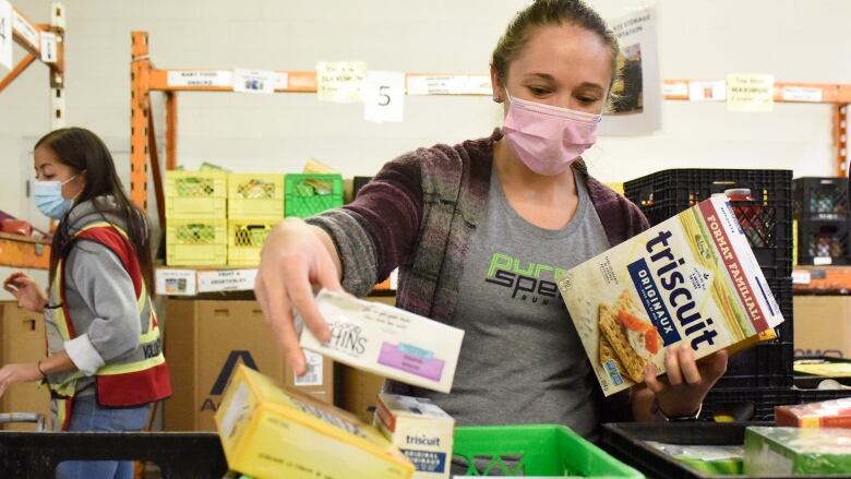 A woman puts food items into a plastic crate.