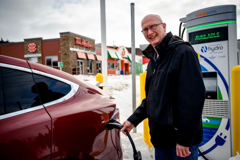 A man smiles as he plugs a charging cable into an electric car.