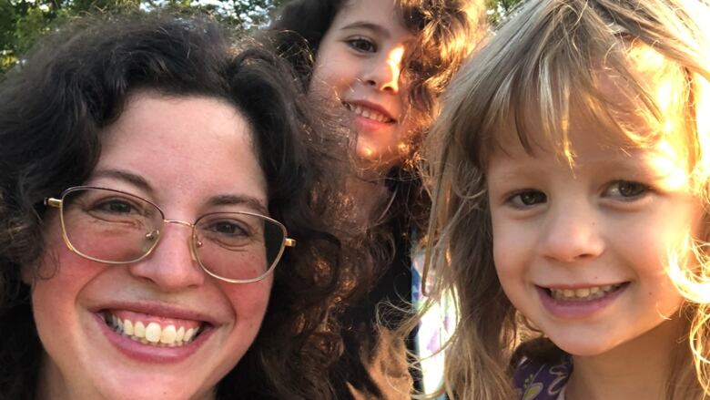 A closeup of woman with curly brown hair and glasses, with two young girls.