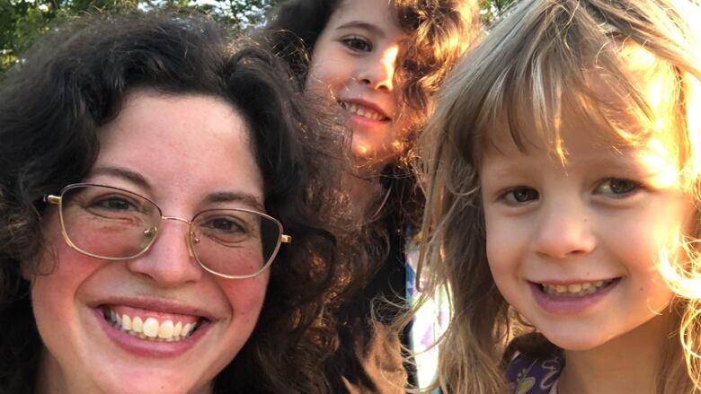 A closeup of woman with curly brown hair and glasses, with two young girls.