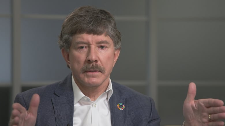 A man in a grey suit speaks with a reporter.