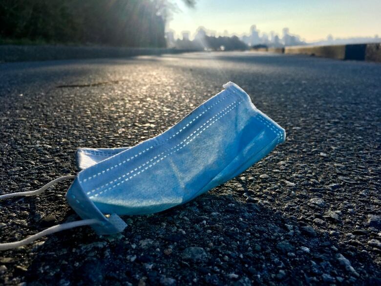 A discarded medical face mask rests on a roadway.