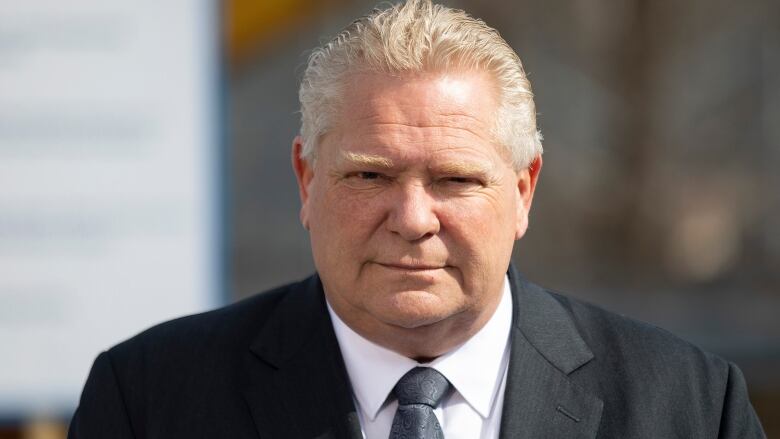 A white-haired man with a slight smile wears a suit