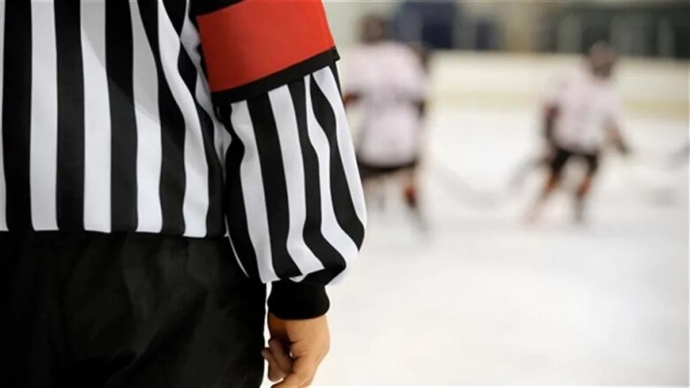 A hockey referee wearing a black and white striped shirt with orange arm bands. 