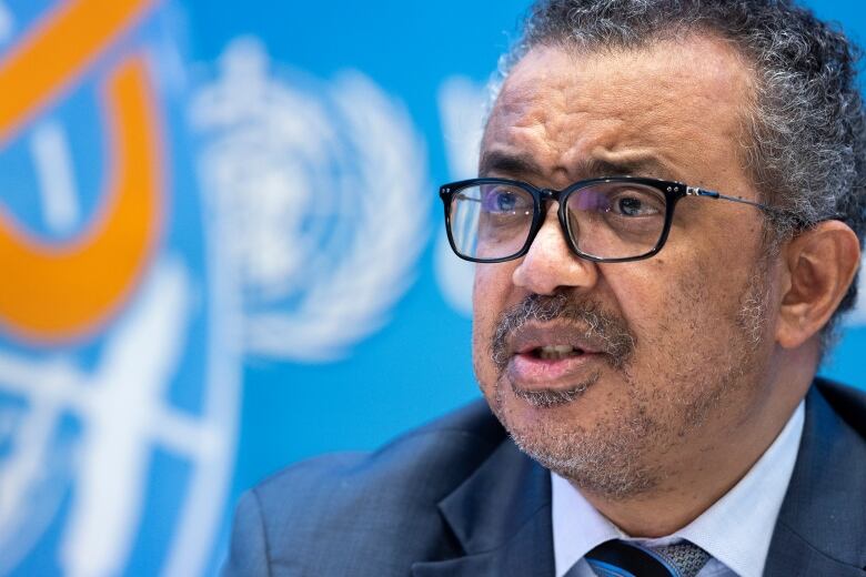 Man in glasses in front of World Health Organization background.