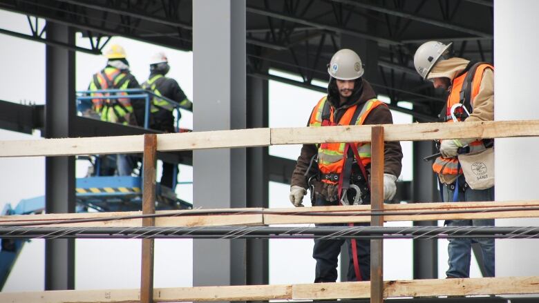 Construction workers in fluorescent orange vests stand on scaffolding while putting up a new building.