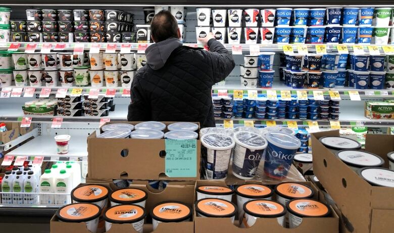 A man facing away from the camera grabs an item from the dairy aisle of a grocery store.